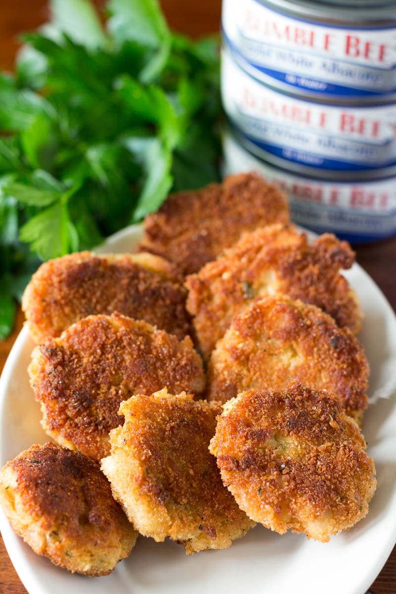 Tuna cakes on a white plate with parsley garnish and cans of tuna