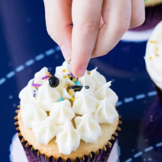 Hand of a child dropping sprinkles on a vanilla cupcake
