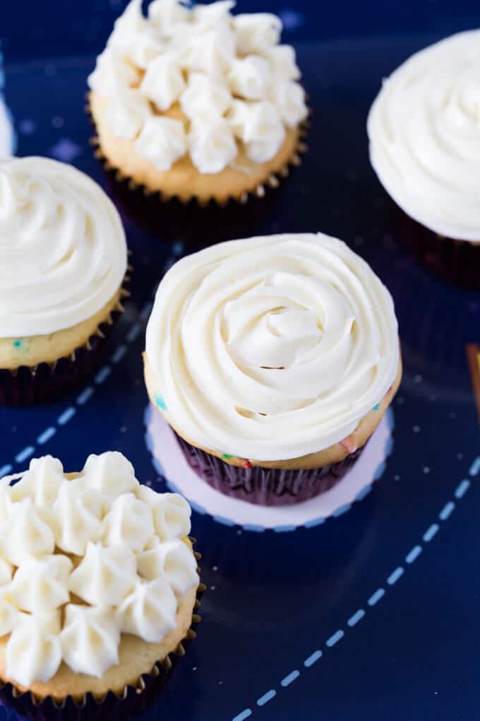 Five vanilla cupcakes with white frosting in different styles