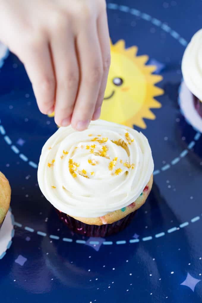 Child's hand sprinkling gold stars on a cupcake