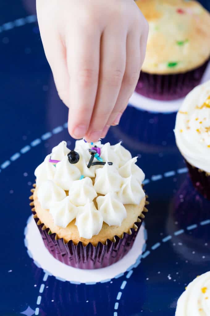 Little girl's hand sprinkling decorations on a cupcake with frosting