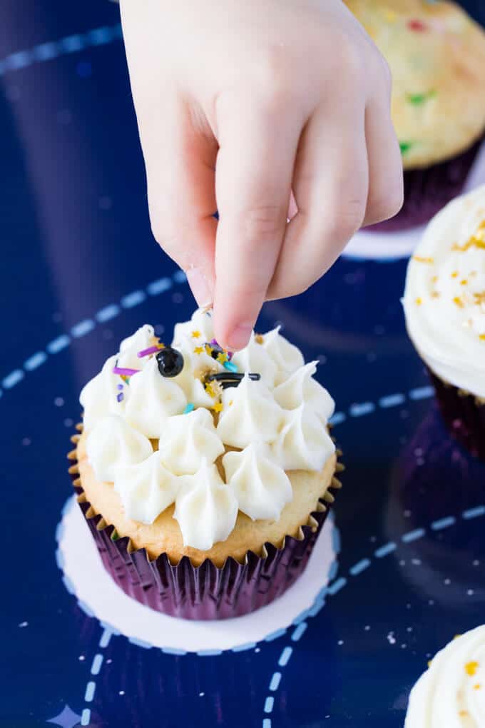 Fingers of a child dropping sprinkles on a cupcake