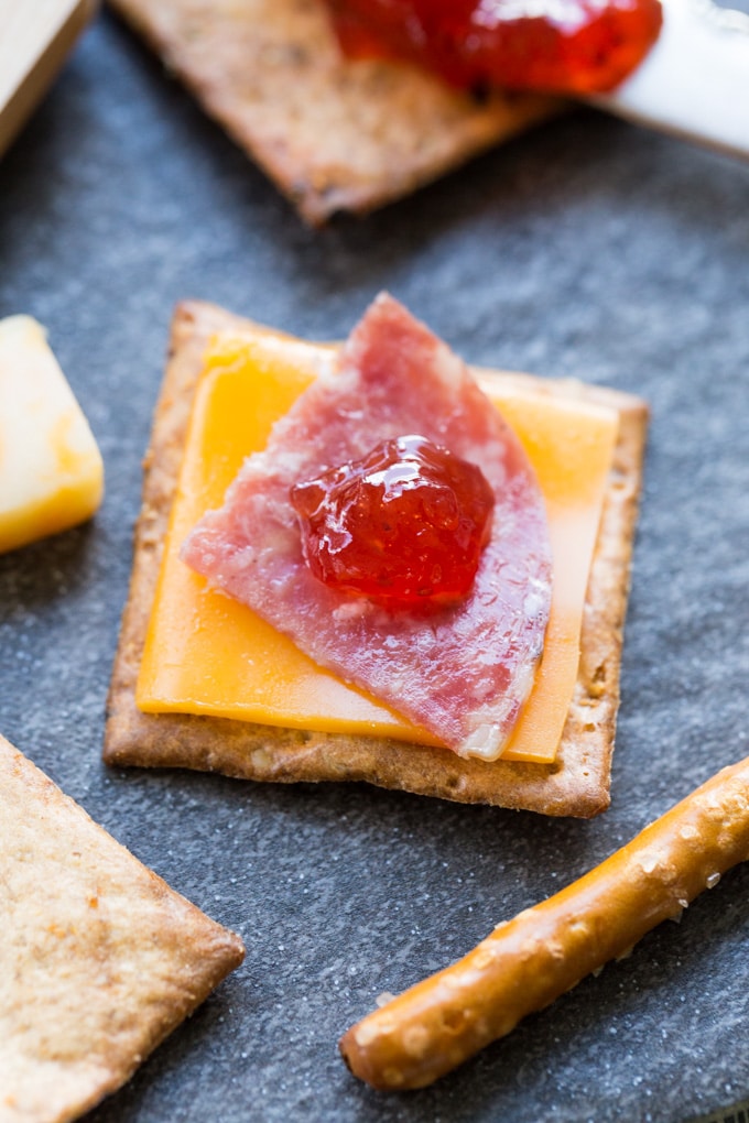 Cracker with American cheese, salami, and strawberry jam on a charcuterie board