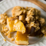 Gluten free apple crisp on a white plate with a wooden serving spoon