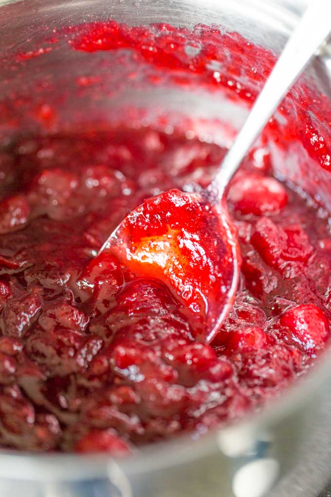 Homemade cranberry sauce being cooking in a stainless steel pot and stirred with a stainless steel spoon