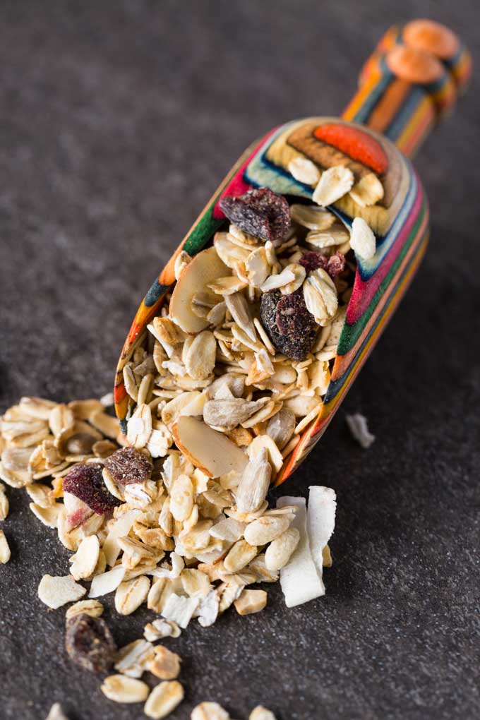 Muesli in a wooden scoop with rainbow colors on a slate background