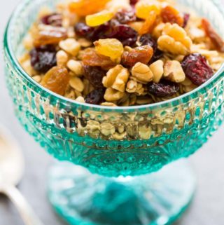 Granola with fruit and nuts in a teal glass footed bowl with a silver spoon