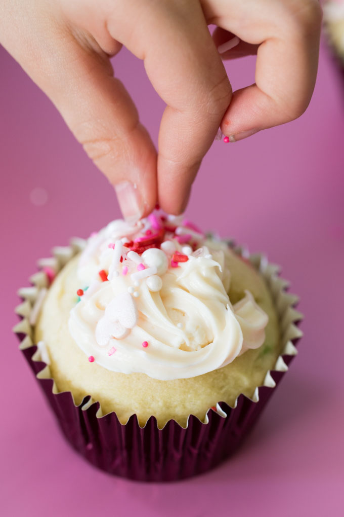 Funfetti cupcake with vanilla frosting being decorated with sprinkles