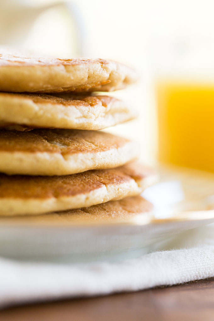 Stack of five oat flour pancakes on a plate and napkin with orange juice