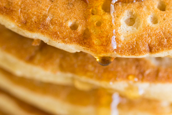 Closeup of maple syrup dripping down a stack of oat flour pancakes