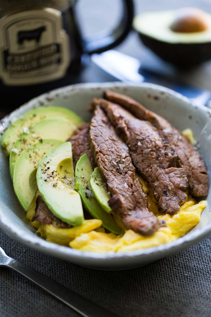 Steak and egg breakfast bowl with fork, mug, and half avocado