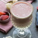 PBJ smoothie in a glass with smoothie ingredients: vanilla frozen yogurt, strawberries, bananas