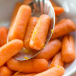 sous vide carrots in a white bowl with serving spoon