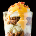 Parfait of mashed potatoes, chili, cheese sauce, and bacon in a glass
