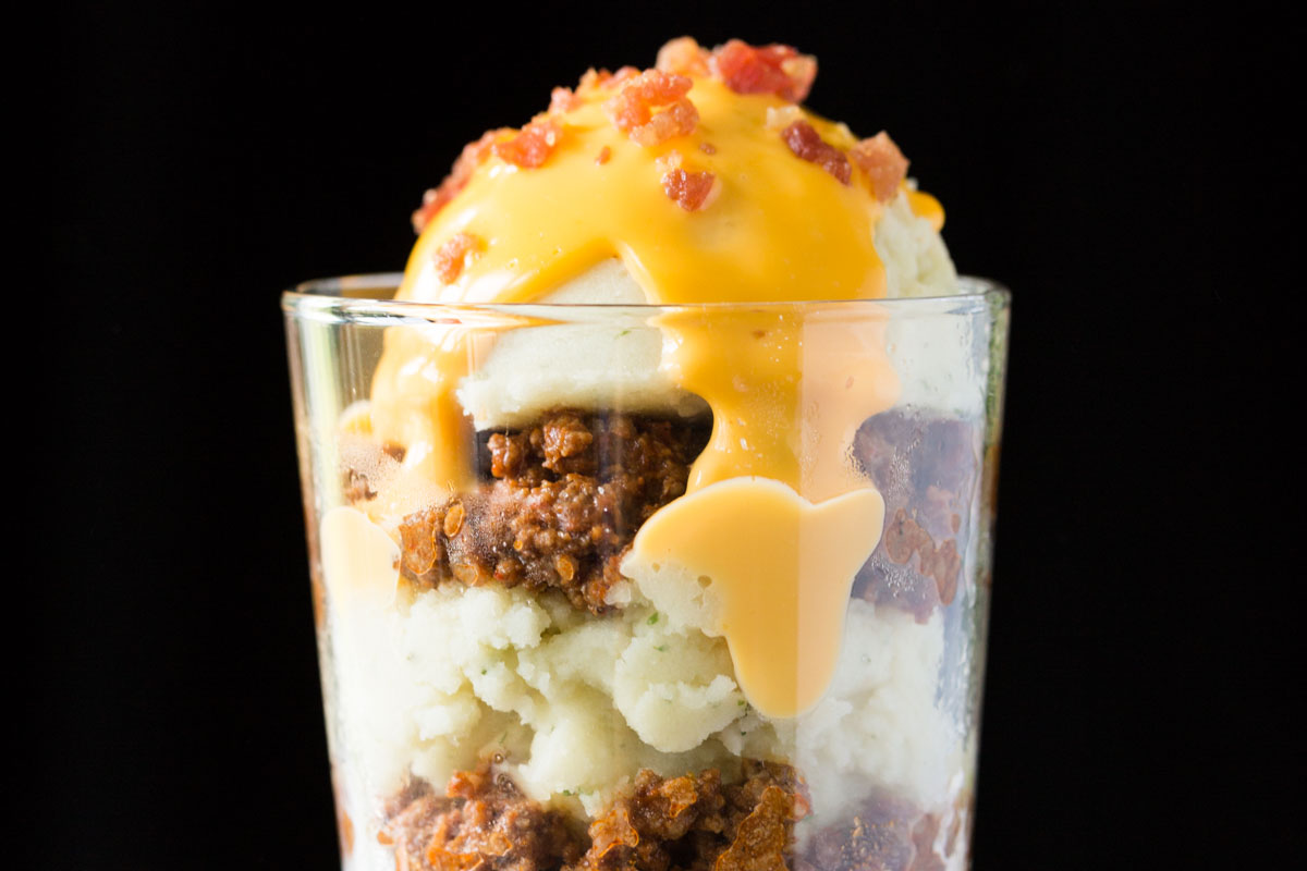 Potato parfait of mashed potatoes, chili, cheese sauce, and bacon in a glass