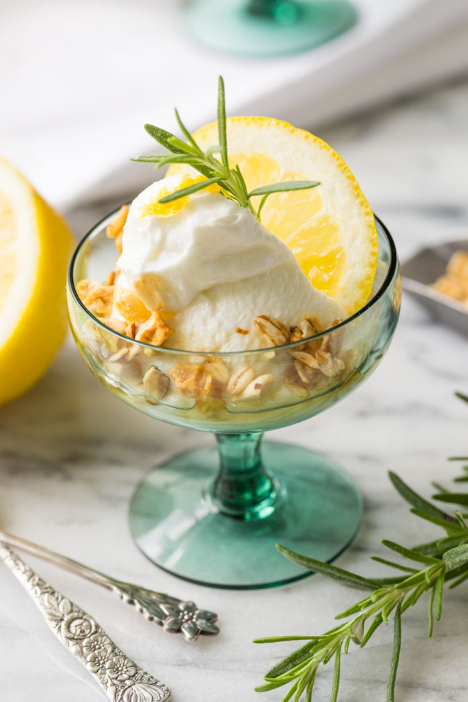 Greek yogurt in a glass with granola, honey, lemon slice, and fresh rosemary
