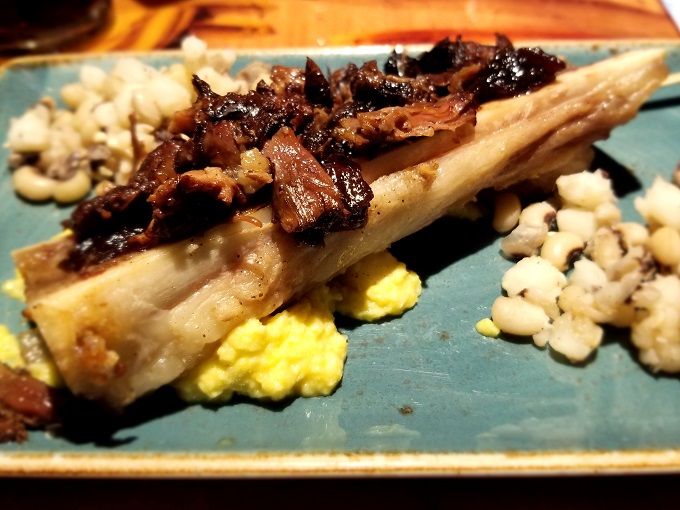 Braised oxtail with marrow, hominy, and beans on a plate at Sanaa restaurant