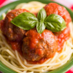 Gluten free meatballs with tomato sauce over gluten free spaghetti in a green bowl