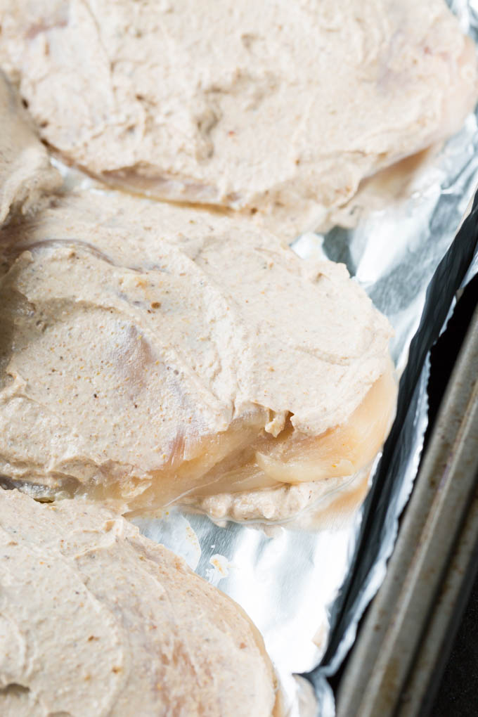 Chicken marinating in Greek yogurt in a baking pan lined with aluminum foil