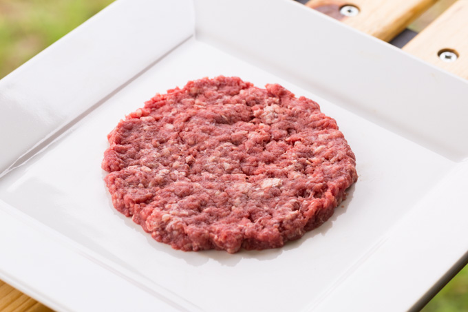 A raw bison burger patty on a square white plate