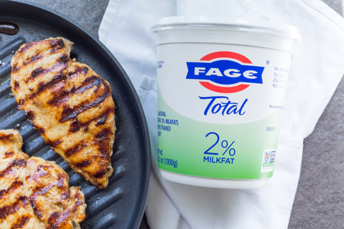 Yogurt marinated chicken breast in a grill pan next to FAGE Total Greek Yogurt container