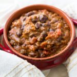 Chili with potatoes in red bowl with off white towel