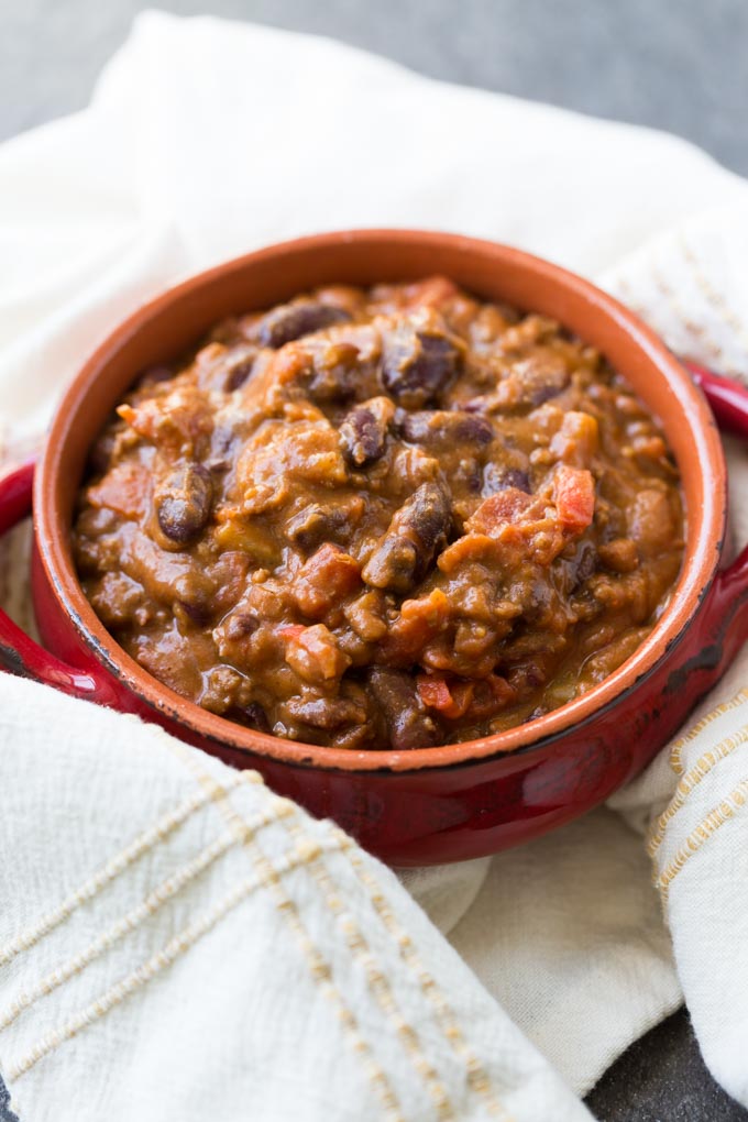 Chili with potatoes in red bowl with off white towel