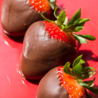 Three chocolate covered strawberries on a red plate