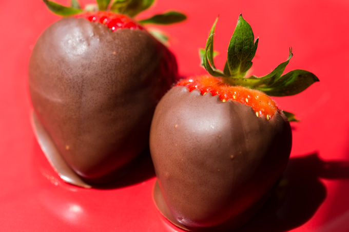 Two chocolate covered strawberries on a red plate