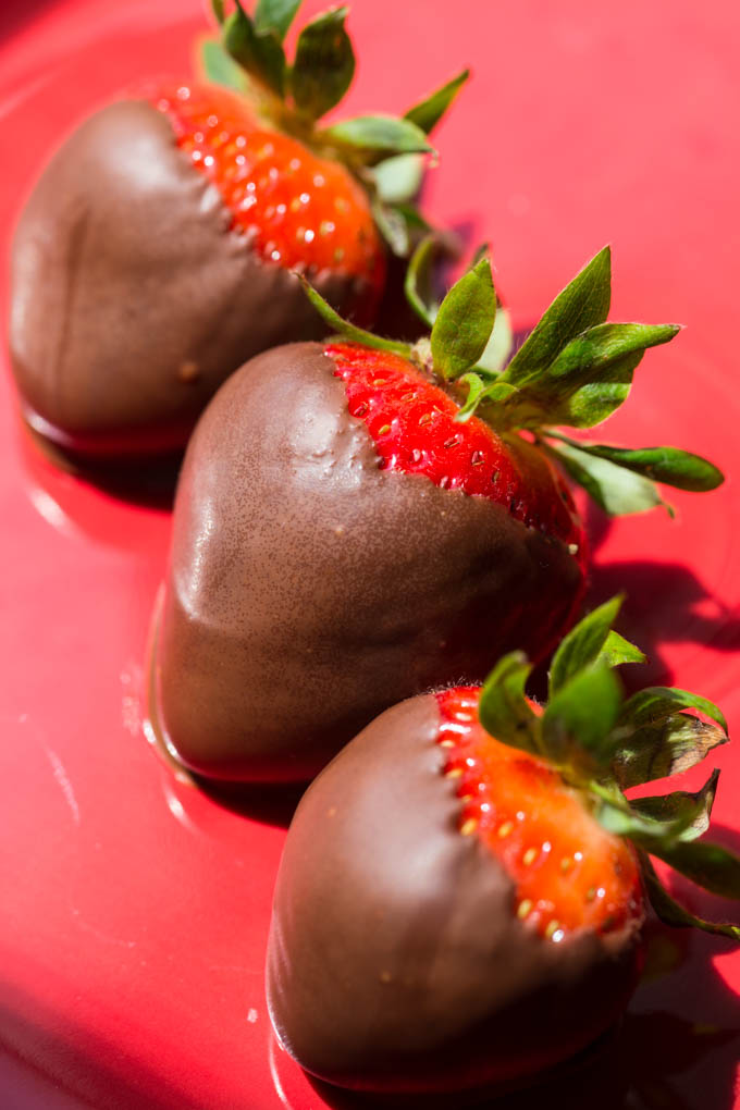 Three chocolate covered strawberries on a red plate